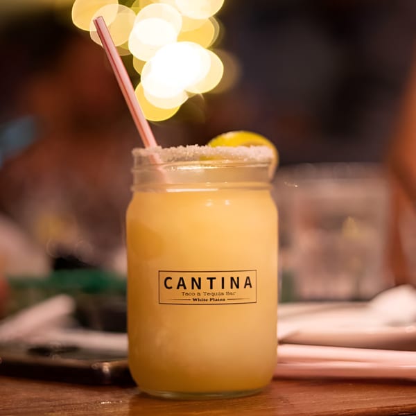 Cantina Taco & Tequila Bar margarita with a straw and lime, against a blurred background.