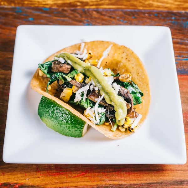 Cantina Taco & Tequila Bar's taco with mushrooms, corn, spinach, cheese, and green sauce, with a lime wedge.