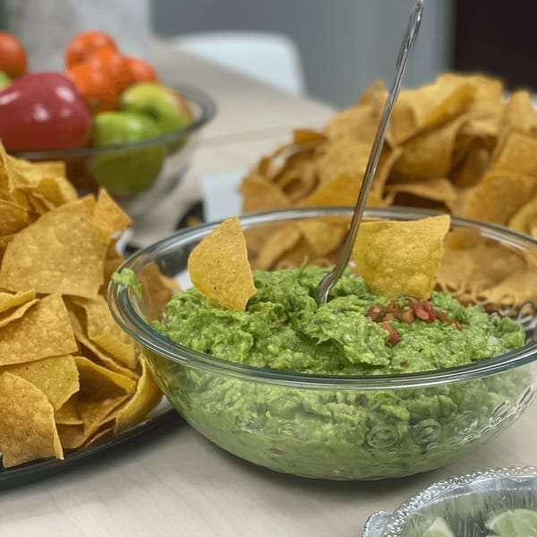 A large glass bowl of guacamole with tortilla chips and a spoon, ready to be served.