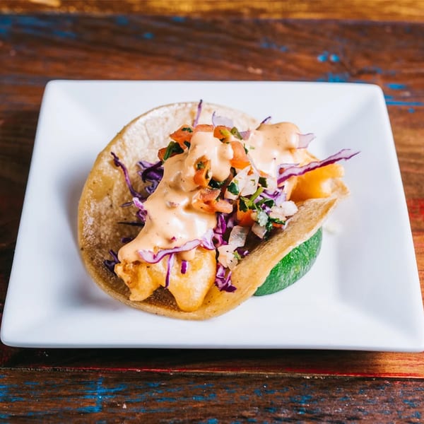 A fish taco from Cantina Taco & Tequila Bar, topped with sauce, pico de gallo, and purple cabbage.