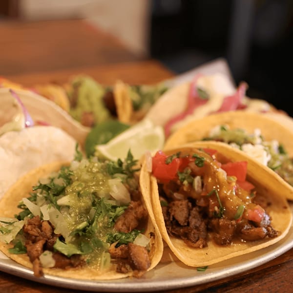 Close-up of several Cantina tacos with various fillings, salsas, and a lime wedge on a platter.