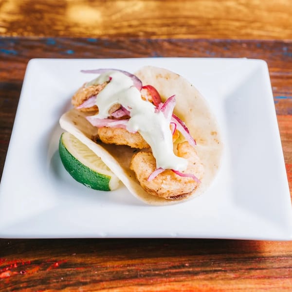 Cantina Taco & Tequila Bar's shrimp taco with red onions, sauce, and a lime wedge.