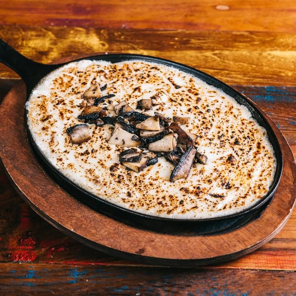 Melted cheese with charred mushrooms in a black skillet on a wooden board at Cantina Taco & Tequila Bar.