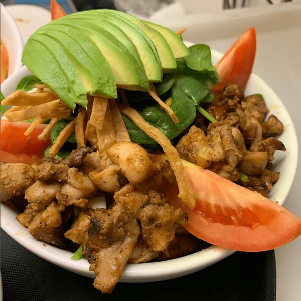 A close-up of a Cantina Taco & Tequila Bar chicken taco salad with avocado, spinach, and tomatoes.