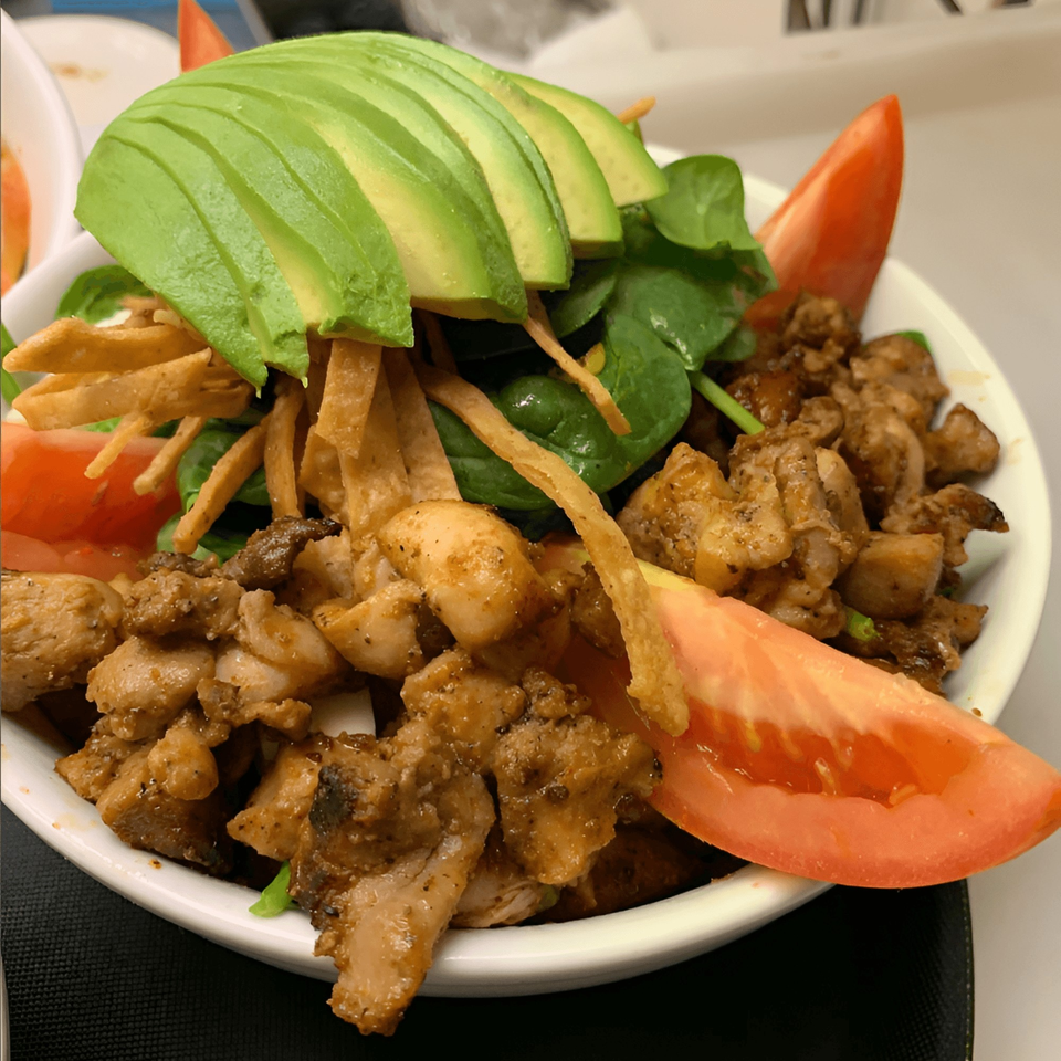A close-up of a Cantina Taco & Tequila Bar chicken taco salad with avocado, spinach, and tomatoes.